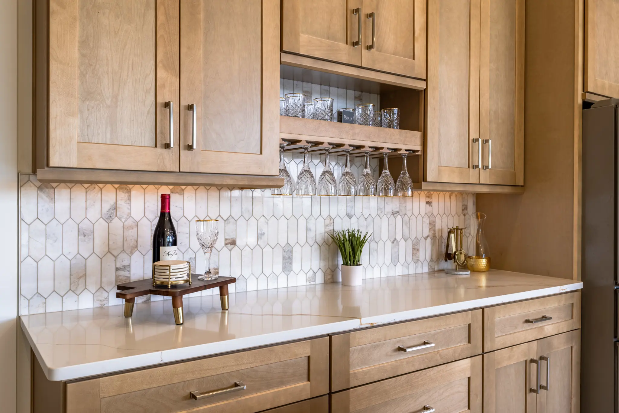 Luxury butler's pantry and wine bar with crystal glassware, marble backsplash, and natural wood cabinets